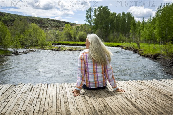 Caucasian woman sitting on dock at river