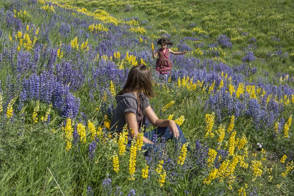 Caucasian mother watching daughter running on hillside with wildflowers