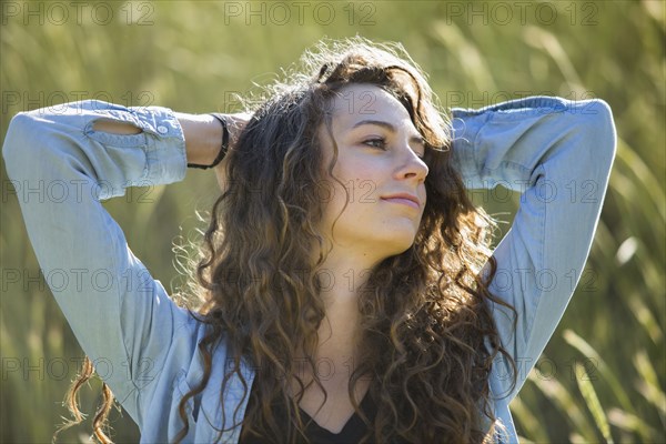 Carefree Caucasian woman with hands behind head in field of tall grass