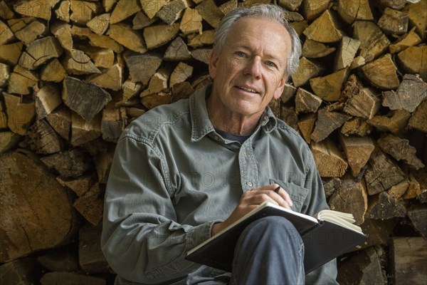 Caucasian man leaning on woodpile writing in journal