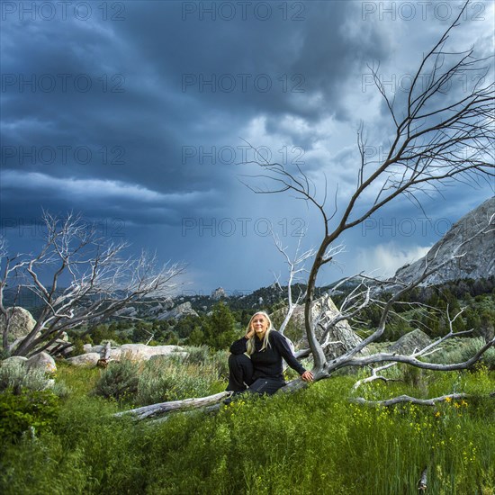 Caucasian woman sitting on fallen tree under clouds