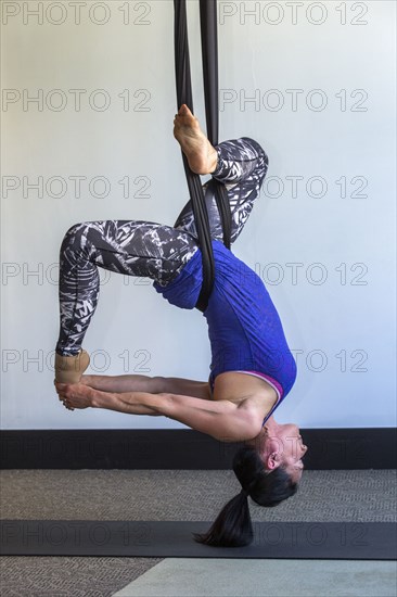 Mixed race woman performing yoga hanging from silks