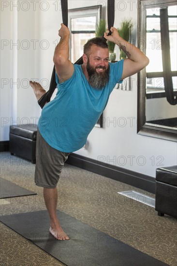 Caucasian man performing yoga hanging from silks