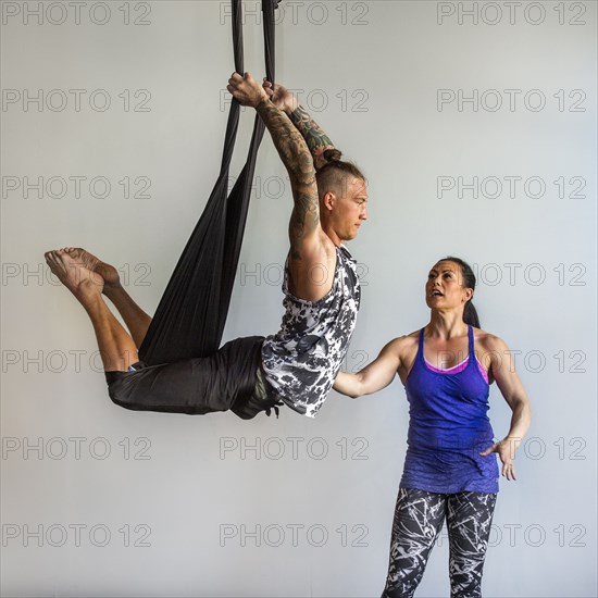 Mixed Race instructor assisting student hanging from silks