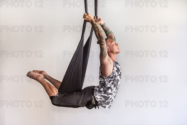 Mixed Race man performing yoga hanging from silks