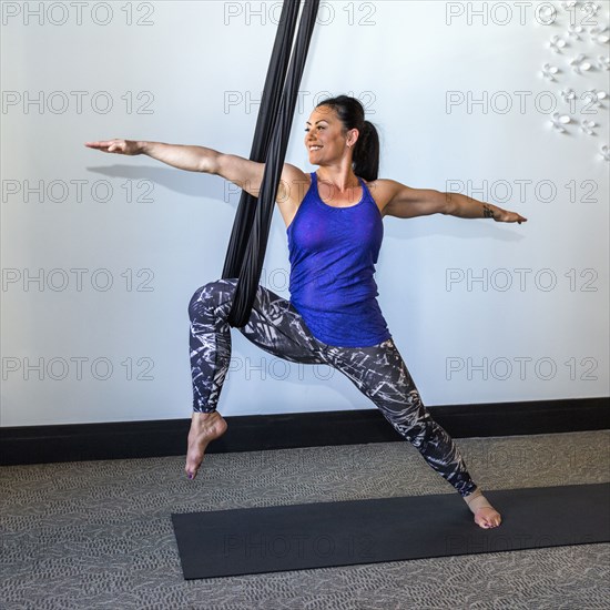 Mixed Race woman performing yoga hanging from silks