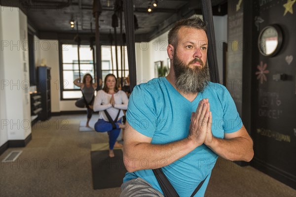 Caucasian man meditating hanging from silks