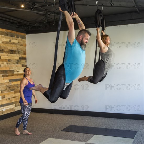 Instructor watching students performing yoga hanging from silks