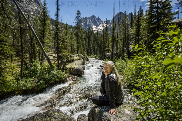 Smiling Caucasian woman sitting on rock at mountain river