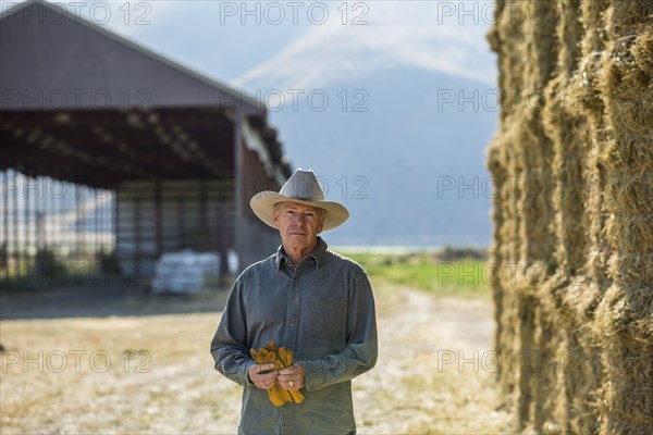 Caucasian farmer holding gloves near stacks of hay