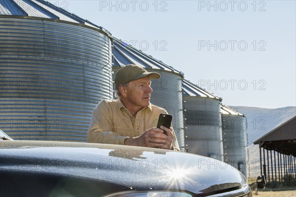 Caucasian farmer leaning on truck texting on cell phone