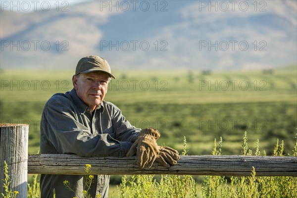 Caucasian farmer wearing gloves leaning on wooden fence