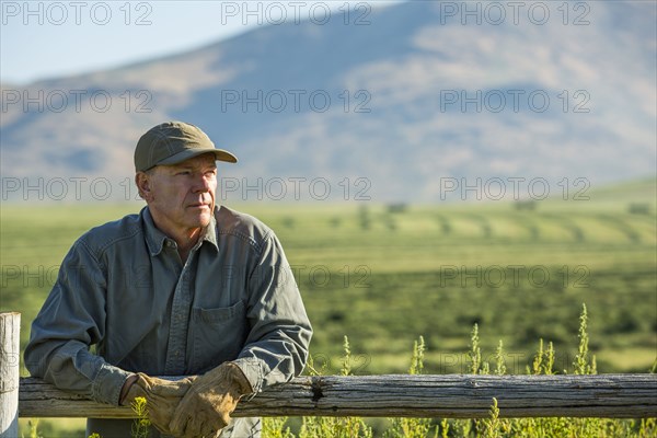 Caucasian farmer wearing gloves leaning on wooden fence