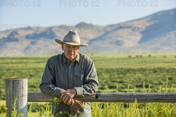 Caucasian farmer holding gloves leaning on wooden fence