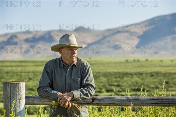 Caucasian farmer holding gloves leaning on wooden fence