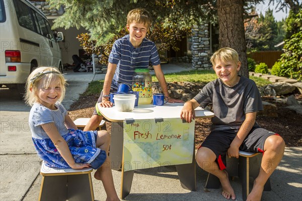 Smiling Caucasian boys and girl selling lemonade