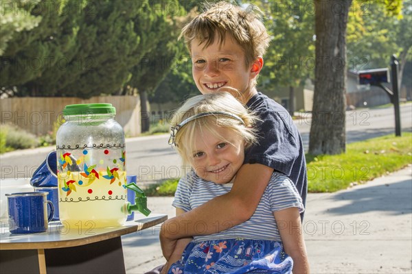 Smiling Caucasian boy hugging girl and selling lemonade