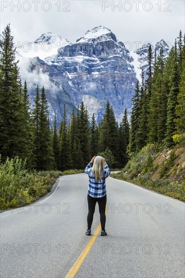 Caucasian woman standing in road photographing mountain