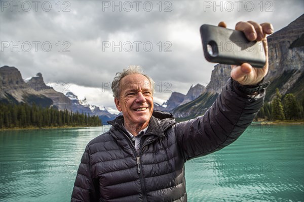 Caucasian man posing for cell phone selfie near mountain lake