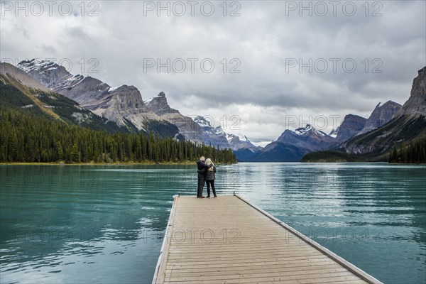 Caucasian couple standing at the end of dock on mountain lake