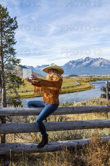 Caucasian woman sitting on wooden fence posing for selfie