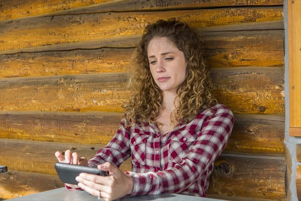 Caucasian woman leaning on wooden wall texting on cell phone