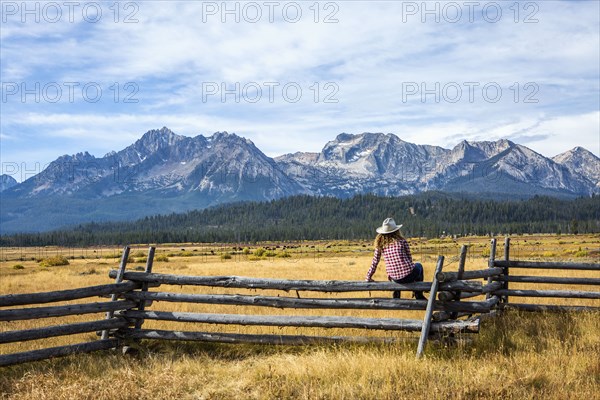 Caucasian woman sitting on wooden fence near mountain river