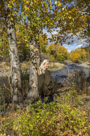 Smiling Caucasian woman leaning on tree near river