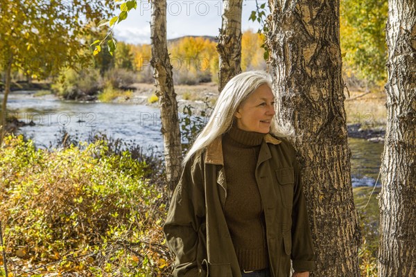 Smiling Caucasian woman leaning on tree near river