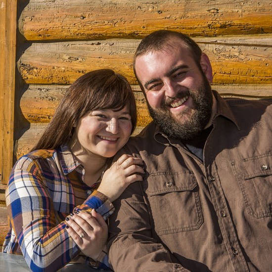 Caucasian couple smiling near log cabin wall