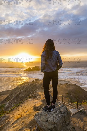 Caucasian woman standing on rock near ocean at sunset