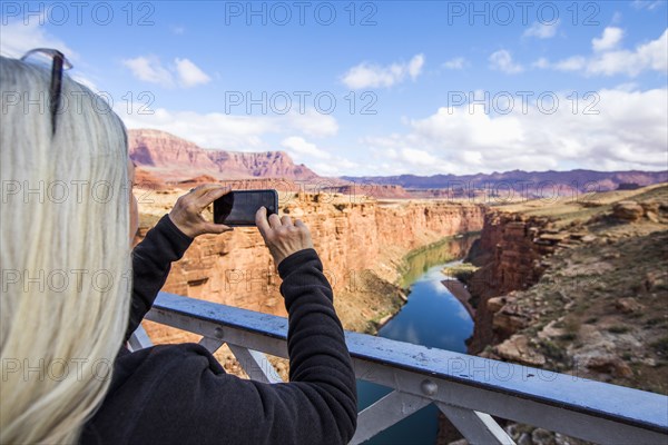 Caucasian woman photographing canyon river with cell phone