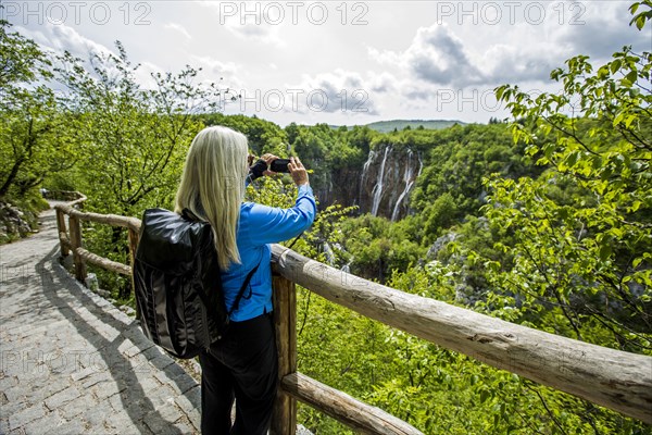 Older Caucasian woman photographing waterfalls with cell phone