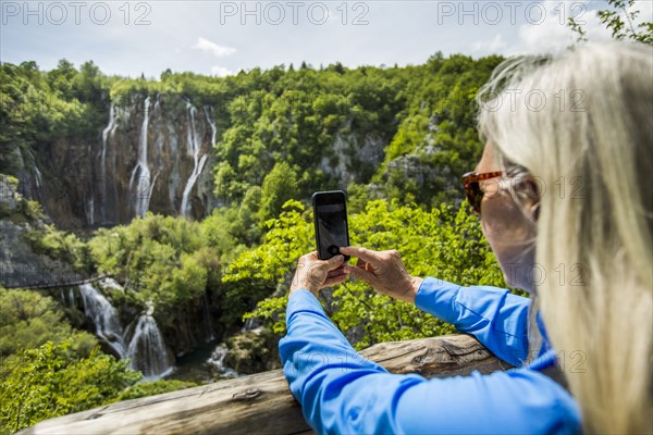 Older Caucasian woman photographing waterfalls with cell phone
