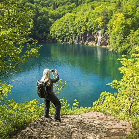 Older Caucasian woman photographing waterfall with cell phone