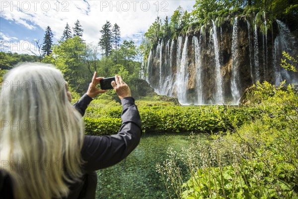 Older Caucasian woman photographing waterfall with cell phone