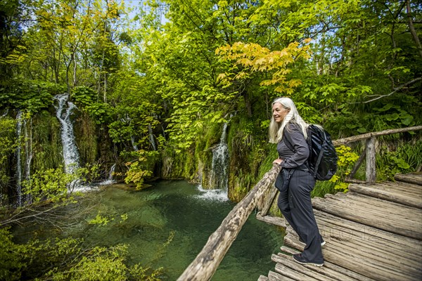 Older Caucasian woman on wooden bridge admiring waterfalls