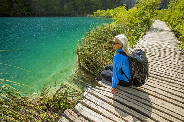 Older Caucasian woman sitting on wooden pathway near water