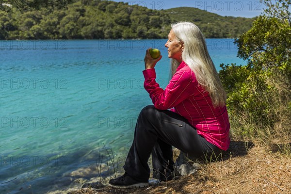 Caucasian woman sitting at lake eating apple