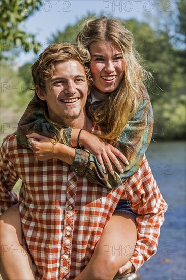 Caucasian boy carrying girl piggyback at river