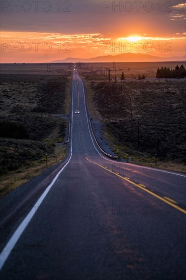 Cars driving on remote road at sunset