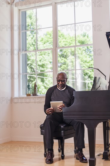 Man sitting at piano using digital tablet near window