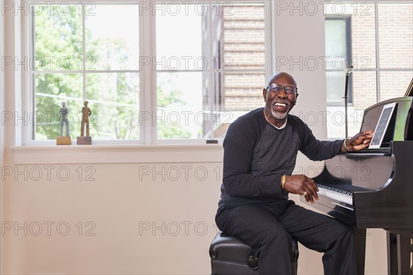 Man sitting at piano with digital tablet near window