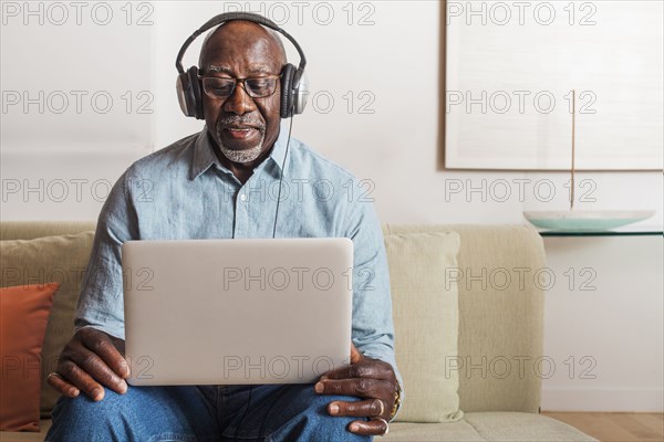Man sitting on sofa listening to laptop with headphones
