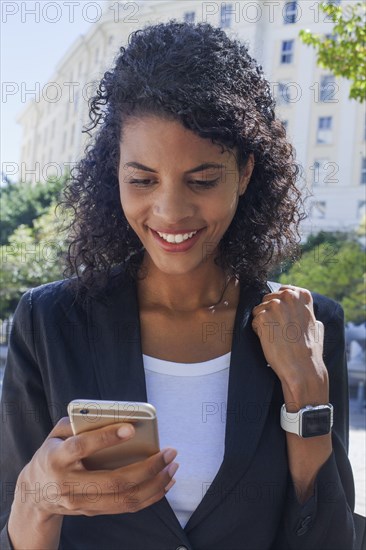 Mixed Race businesswoman texting on cell phone outdoors