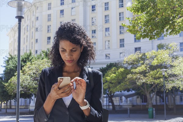 Mixed Race businesswoman texting on cell phone outdoors