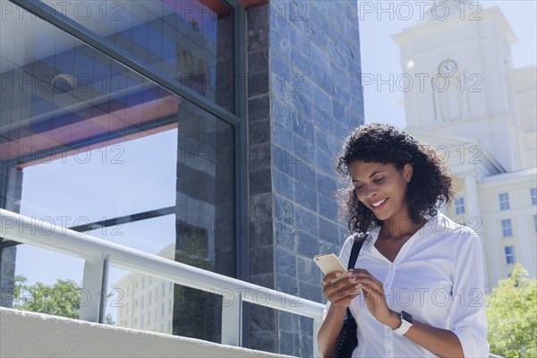 Mixed Race businesswoman texting on cell phone outdoors