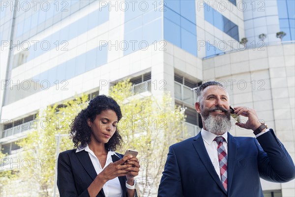 Business people using cell phones near office building