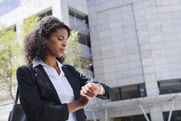 Mixed Race businesswoman checking wristwatch outdoors