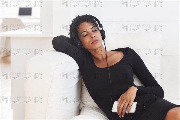 Mixed Race woman on sofa listening to cell phone with headphones